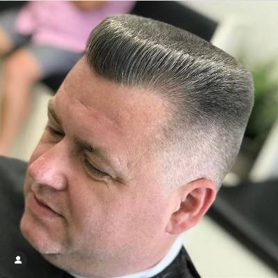 A man with a flat top haircut, featuring a high, voluminous top with a clean fade on the sides, offering a sharp and structured appearance.