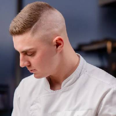 A man with a high and tight military-inspired haircut, featuring very short sides fading into a longer top, offering a clean, structured look.