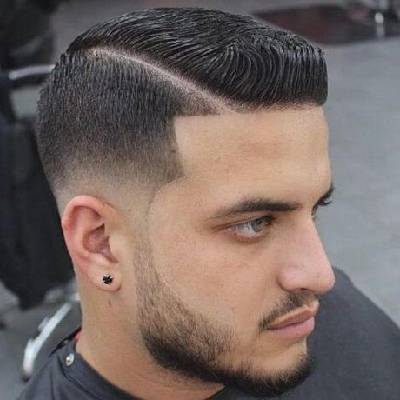 A man with a short pompadour hairstyle, featuring a clean fade on the sides and back, with sleek, well-defined hair on top styled back with a side part.