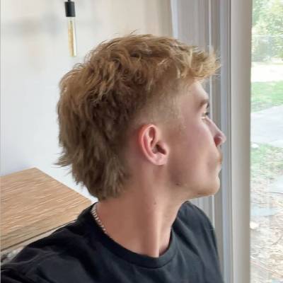 A side profile of a man with a burst fade mullet haircut, showcasing the short sides and longer hair at the back.