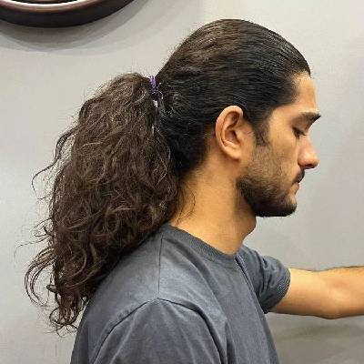 Long curly ponytail hairstyle with natural, voluminous curls tied back neatly for a stylish and relaxed look