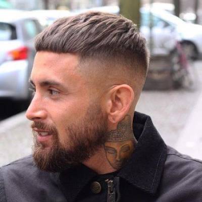 A man with a sharp blunt fringe crop hairstyle featuring faded sides and a short beard.