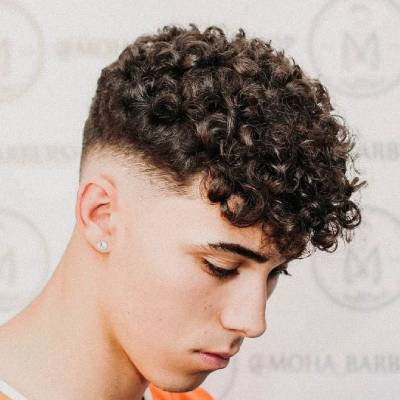 A man with a curly quiff hairstyle, styled with voluminous curls at the front and a fade on the sides.