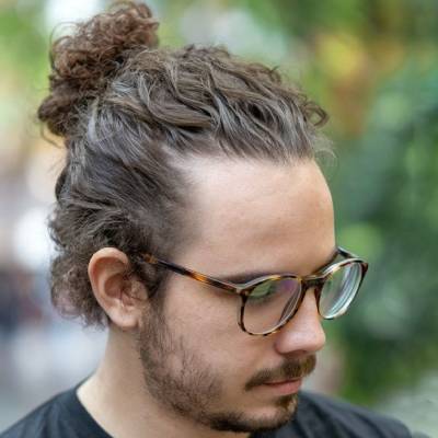 A man with curly hair styled into a man bun, with the sides and back trimmed short, creating a stylish and modern look.