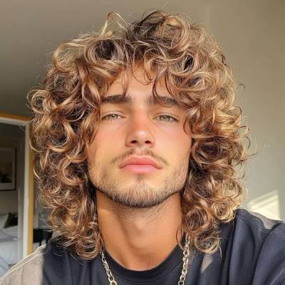 A man with shoulder-length curly hair, styled in voluminous, natural curls for a bold and textured look.