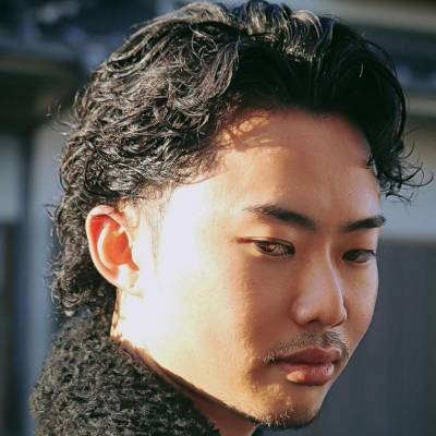 El hombre en la imagen tiene el cabello rizado peinado hacia atrás de manera elegante. El estilo es sofisticado, con los rizos suavemente controlados y los lados más cortos, creando un look limpio y moderno.








