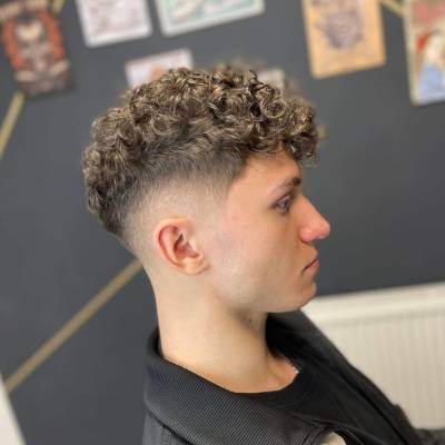 Hombre con corte de cabello francés rizado, con el cabello corto en los lados y rizos naturales en la parte superior.