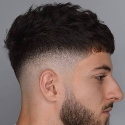 „Profilansicht eines jungen Mannes mit sauberem Fade-Haarschnitt, strukturiertem Oberhaar und gepflegtem Bart.“