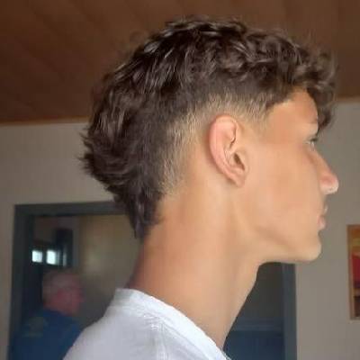 niedrigen Taper-Fade. Die Seiten sind sanft verblasst, während das Haar oben lockig und etwas länger bleibt. Der Mann trägt ein einfaches weißes T-Shirt und hat einen modernen, frischen Look.niedrigen Taper-Fade. Die Seiten sind sanft verblasst, während das Haar oben lockig und etwas länger bleibt. Der Mann trägt ein einfaches weißes T-Shirt und hat einen modernen, frischen Look.