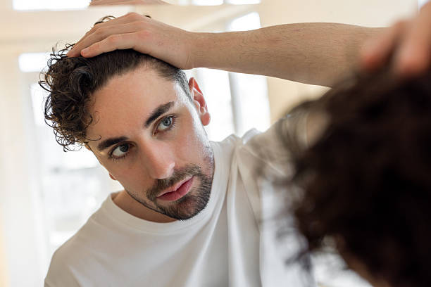 A man closely checking his hair and scalp in the bathroom mirror for dandruff